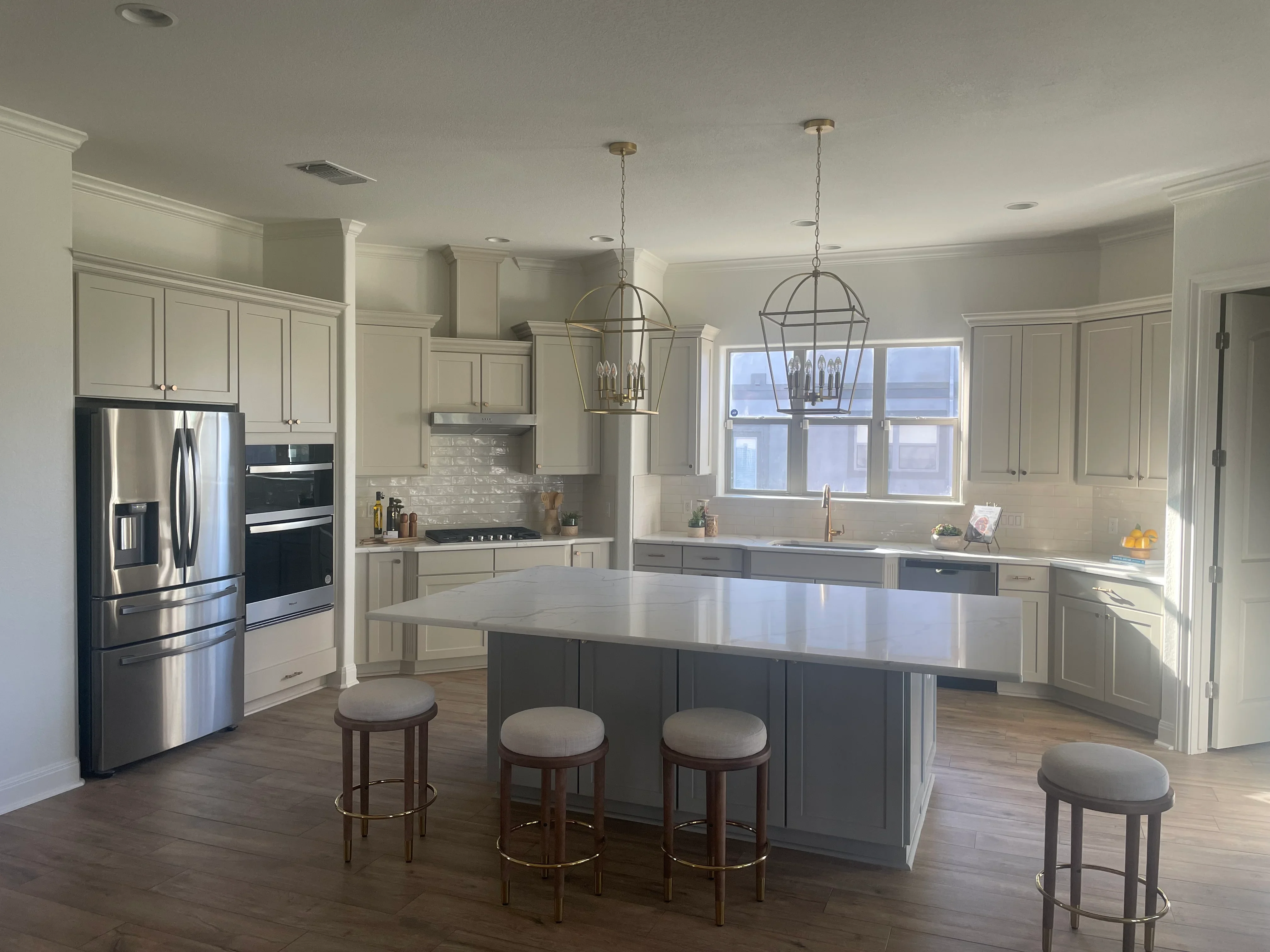 Modern kitchen with cream cabinetry, dark island, quartz counters, stainless appliances, and pendant lights
