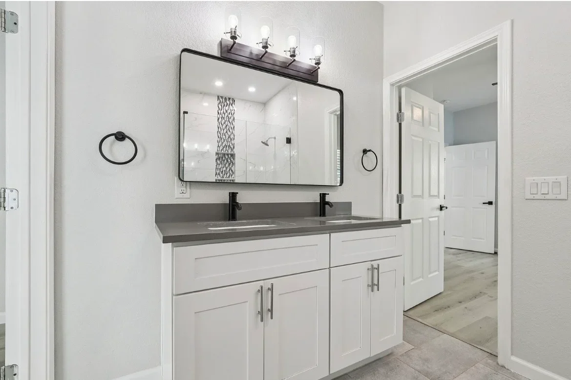 Modern bathroom with white cabinetry, gray quartz countertop, black framed mirror, and dual sinks