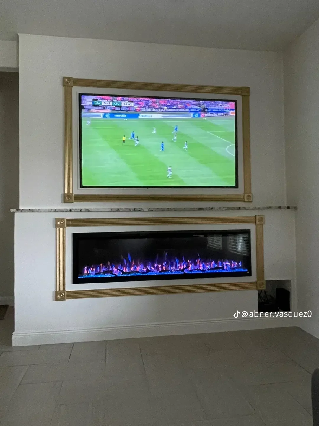 Stacked TV and electric fireplace with brass trim molding on white drywall wall