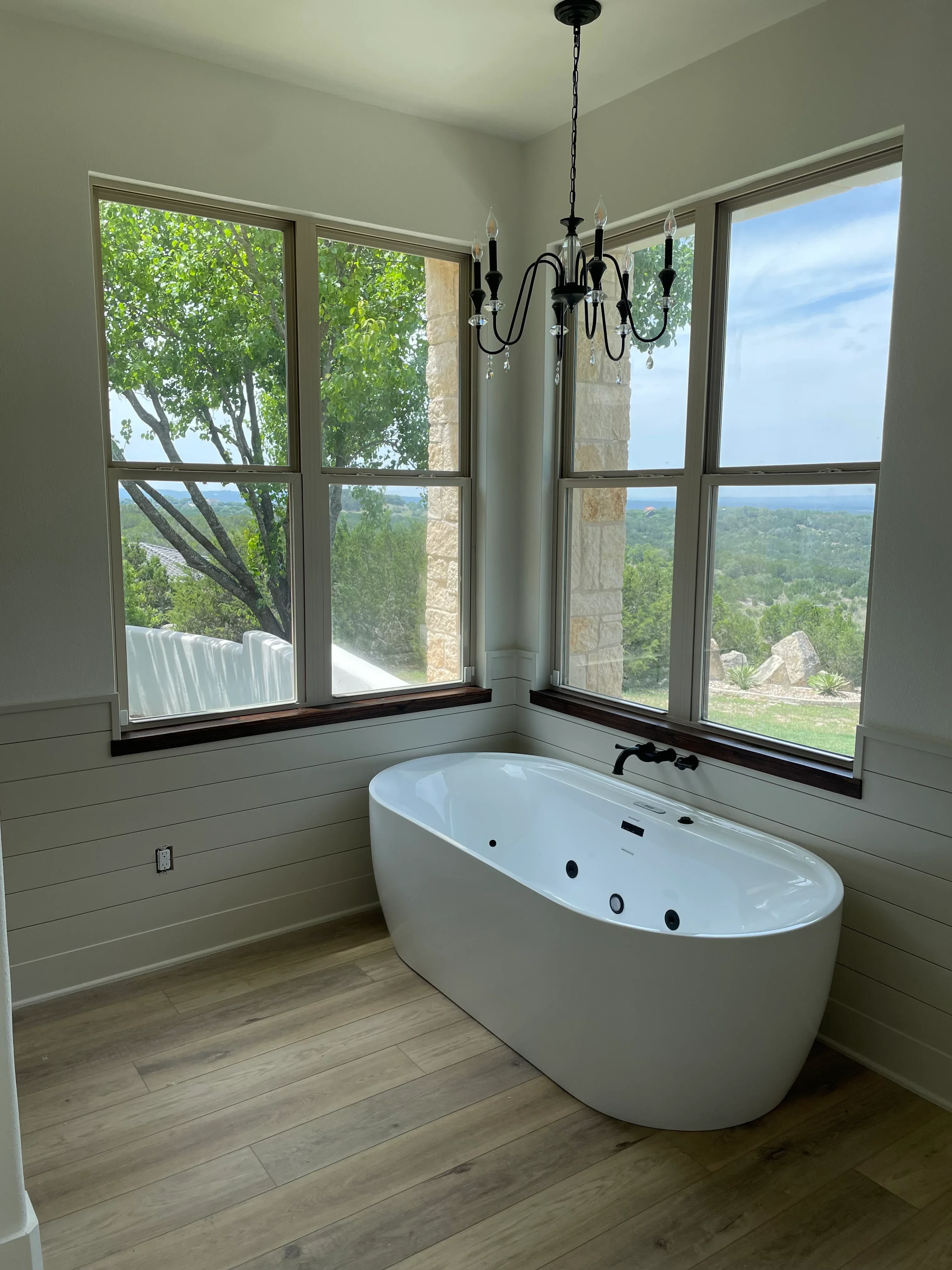 Skylights and multi-pane windows installed in room with white soaking tub and wood flooring