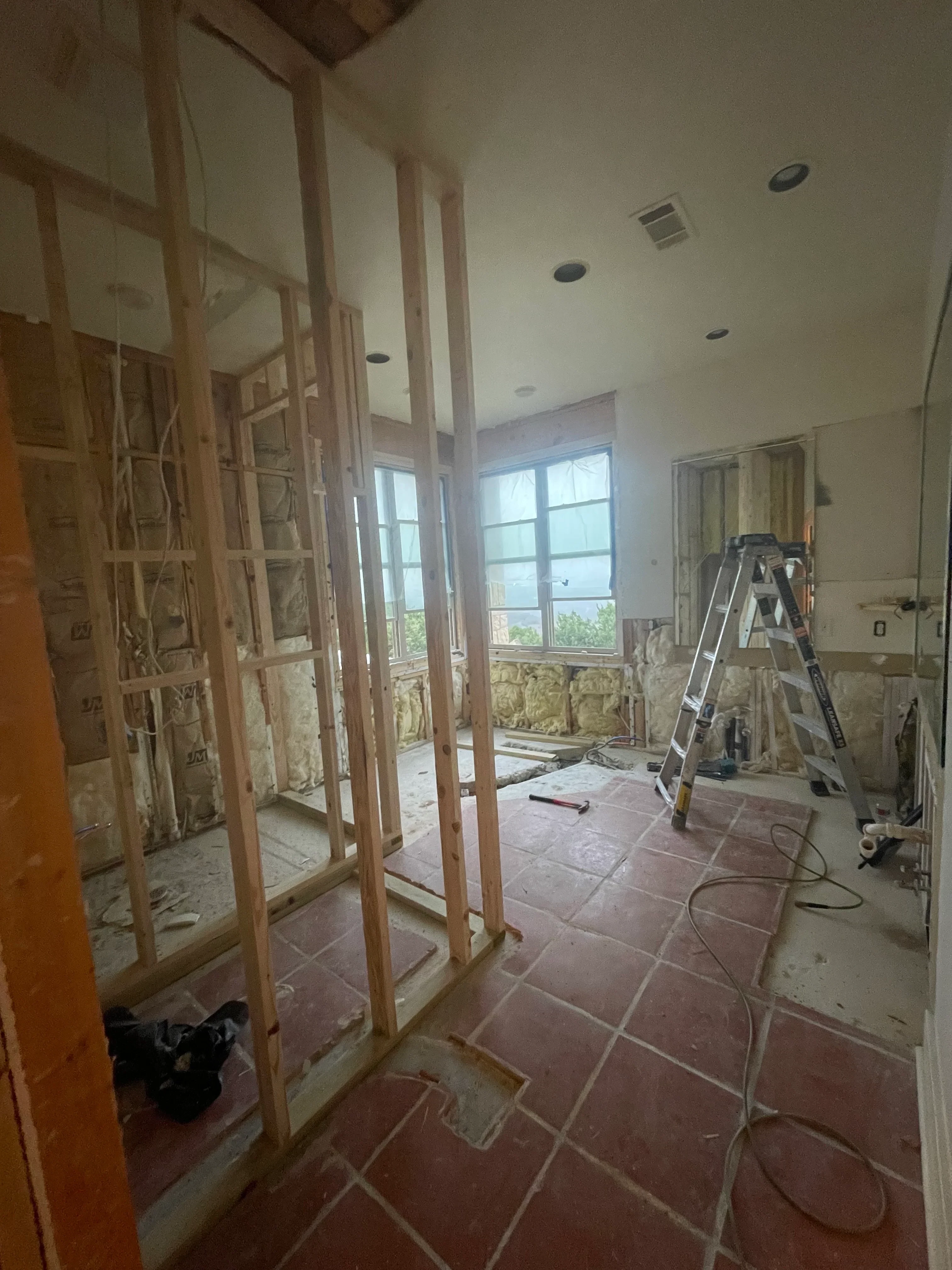 Bathroom renovation in progress with wood framing, drywall, insulation, and red tile wall installation
