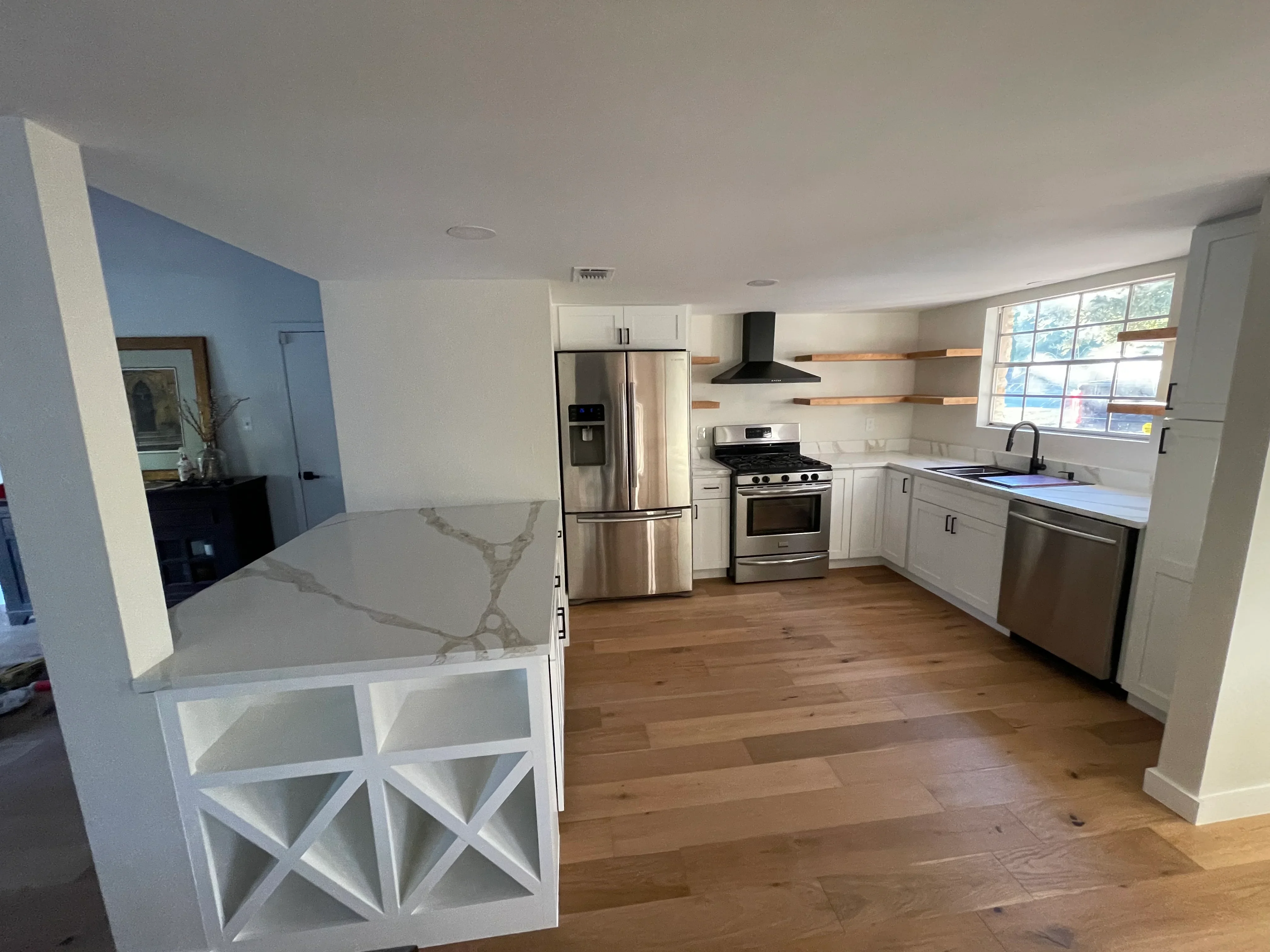 Modern kitchen with white cabinets, stainless steel appliances, quartz island, and hardwood flooring