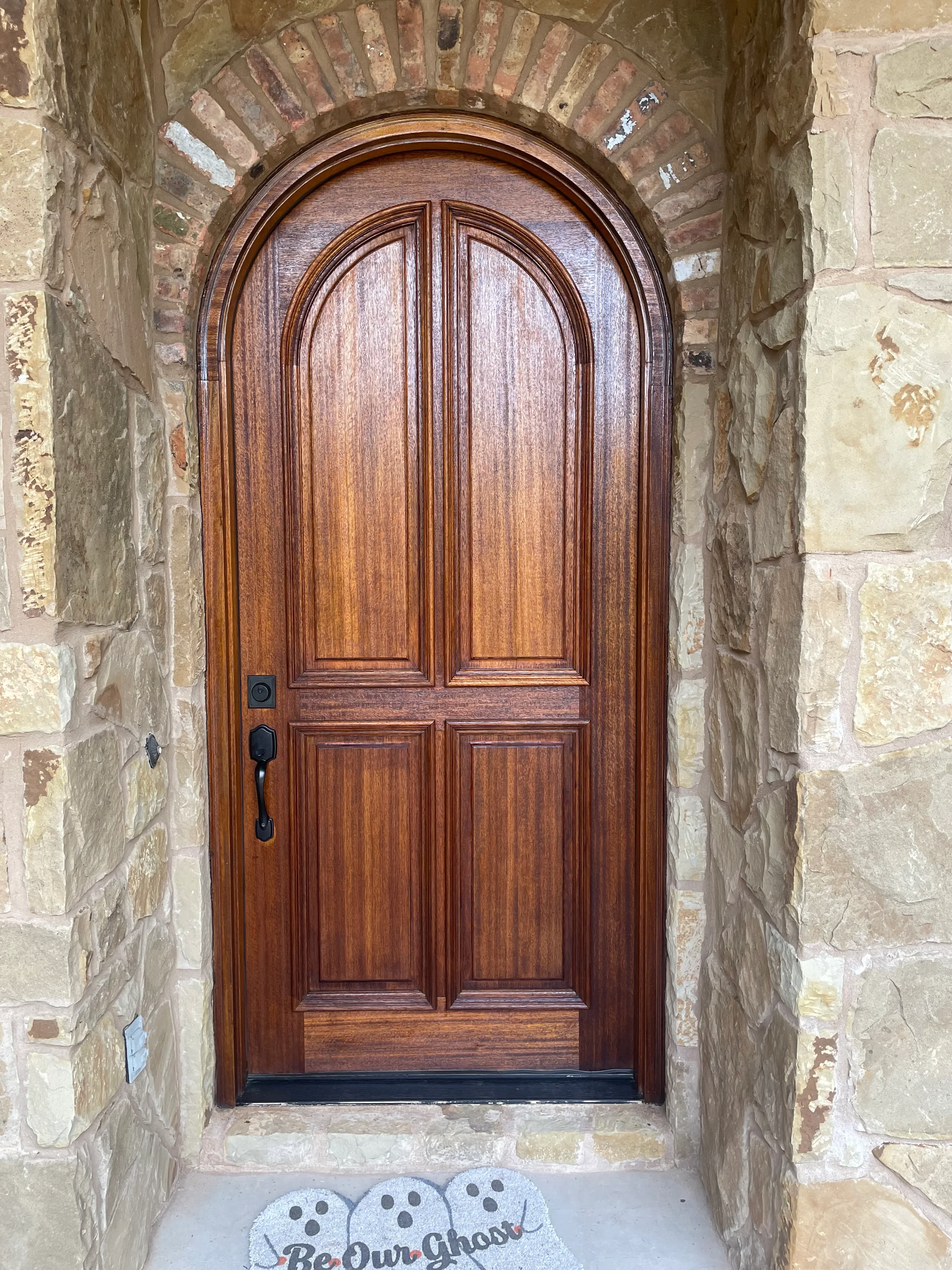 Custom wooden entry door with raised panels and arch detail in stone archway entrance