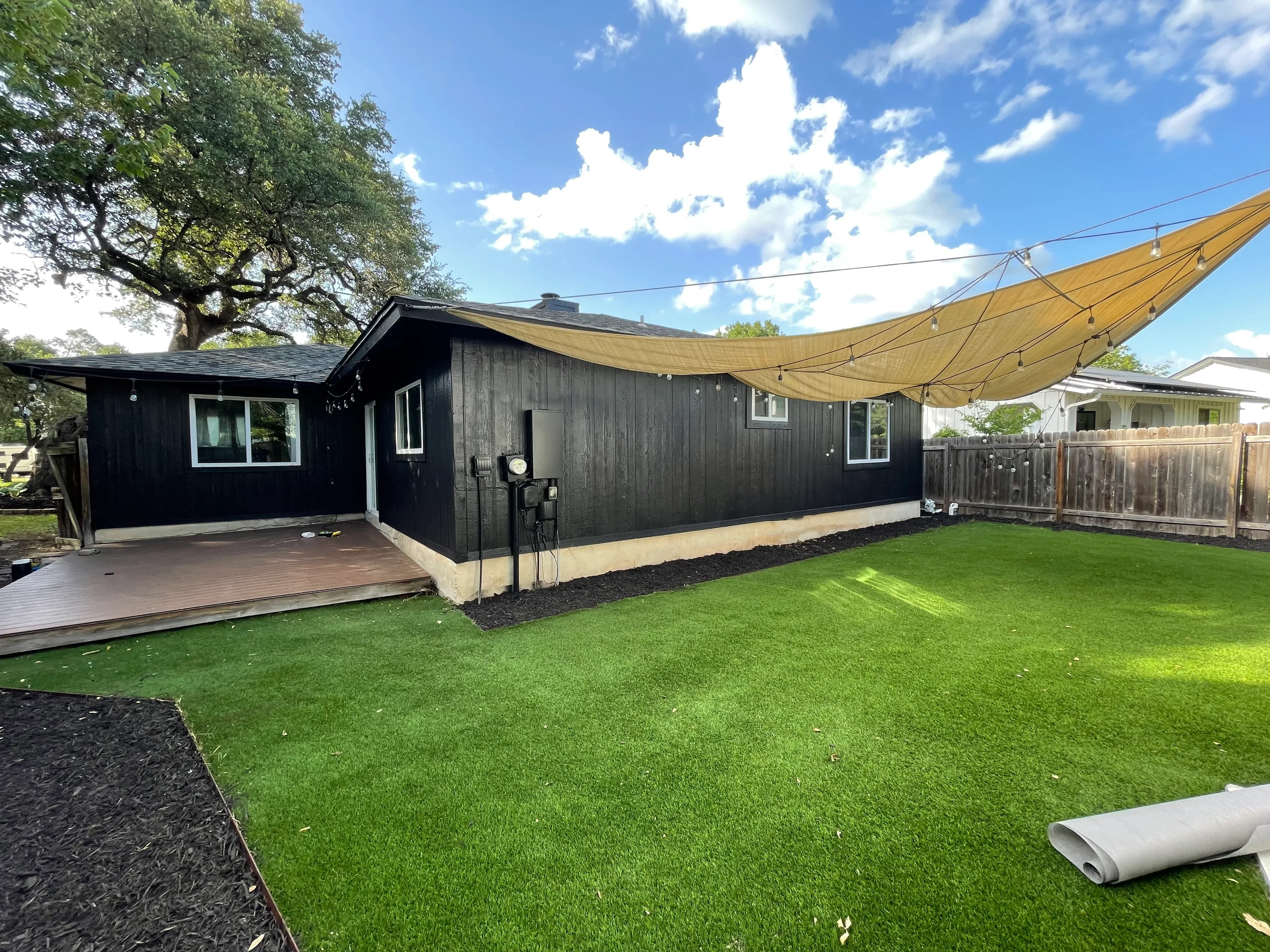 Black siding home with composite deck, shade sail, artificial turf, and mulch landscaping