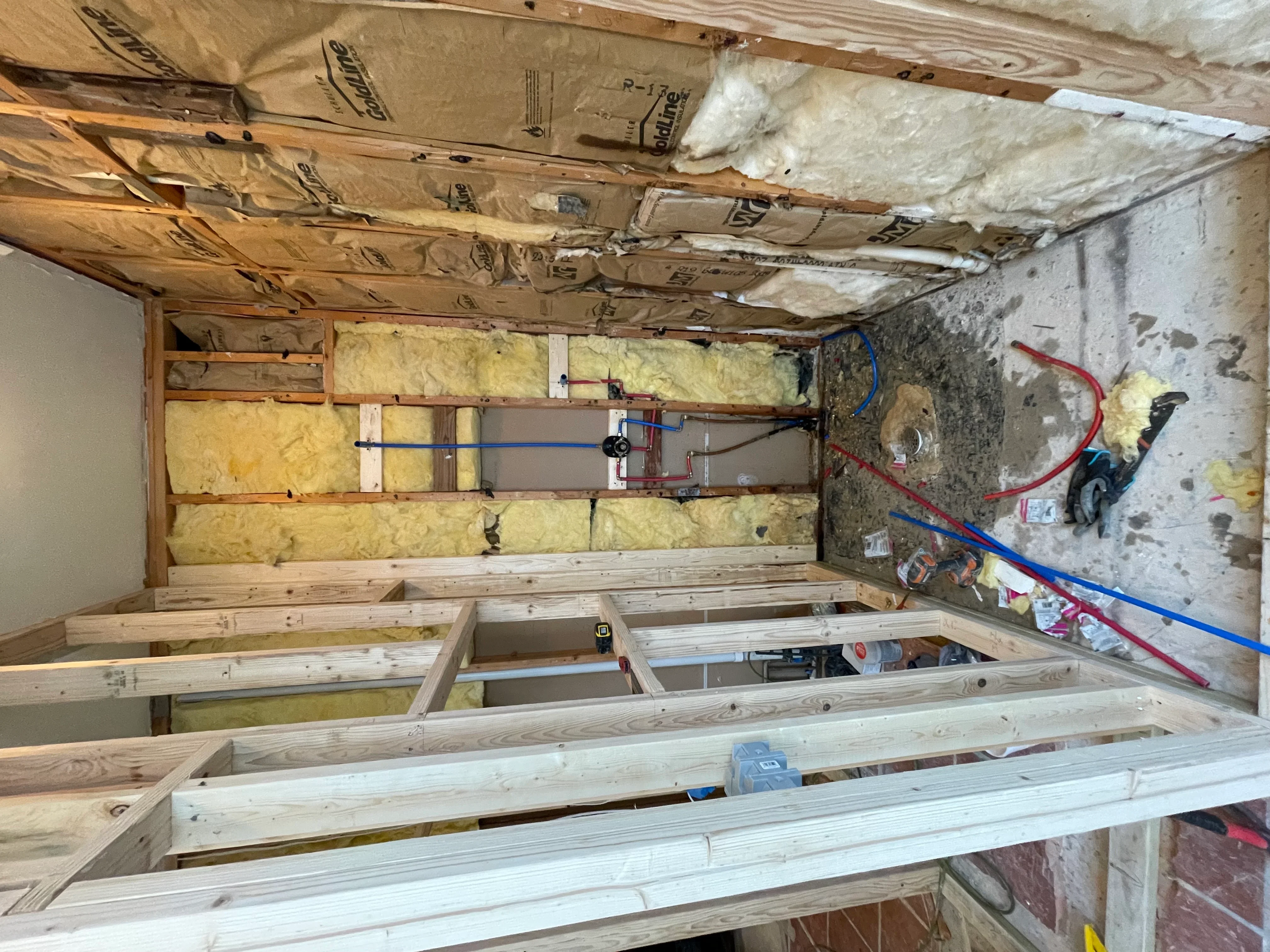 Basement framing with wood joists, fiberglass insulation batts, and electrical/plumbing rough-in
