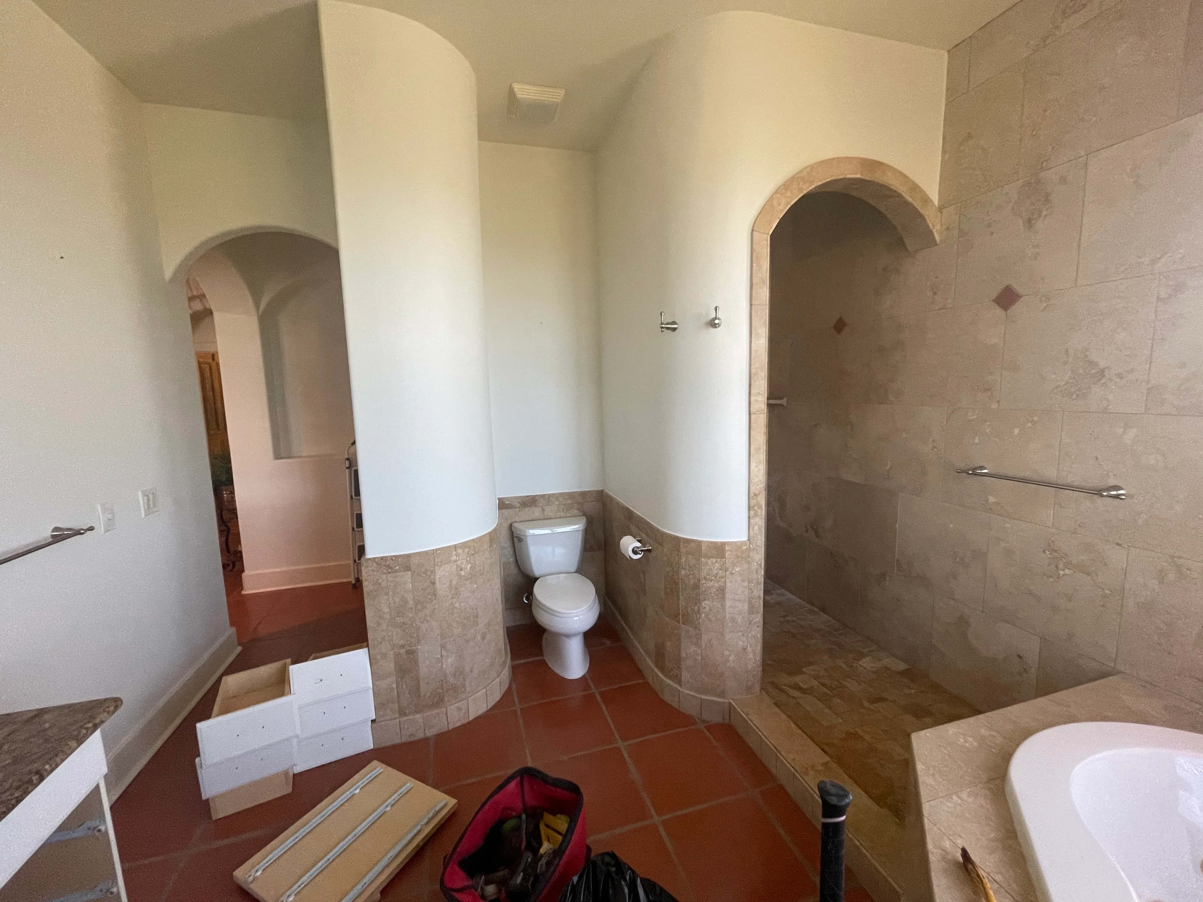 Bathroom with curved archways, travertine tile wainscoting, walk-in shower, and terra cotta tile flooring