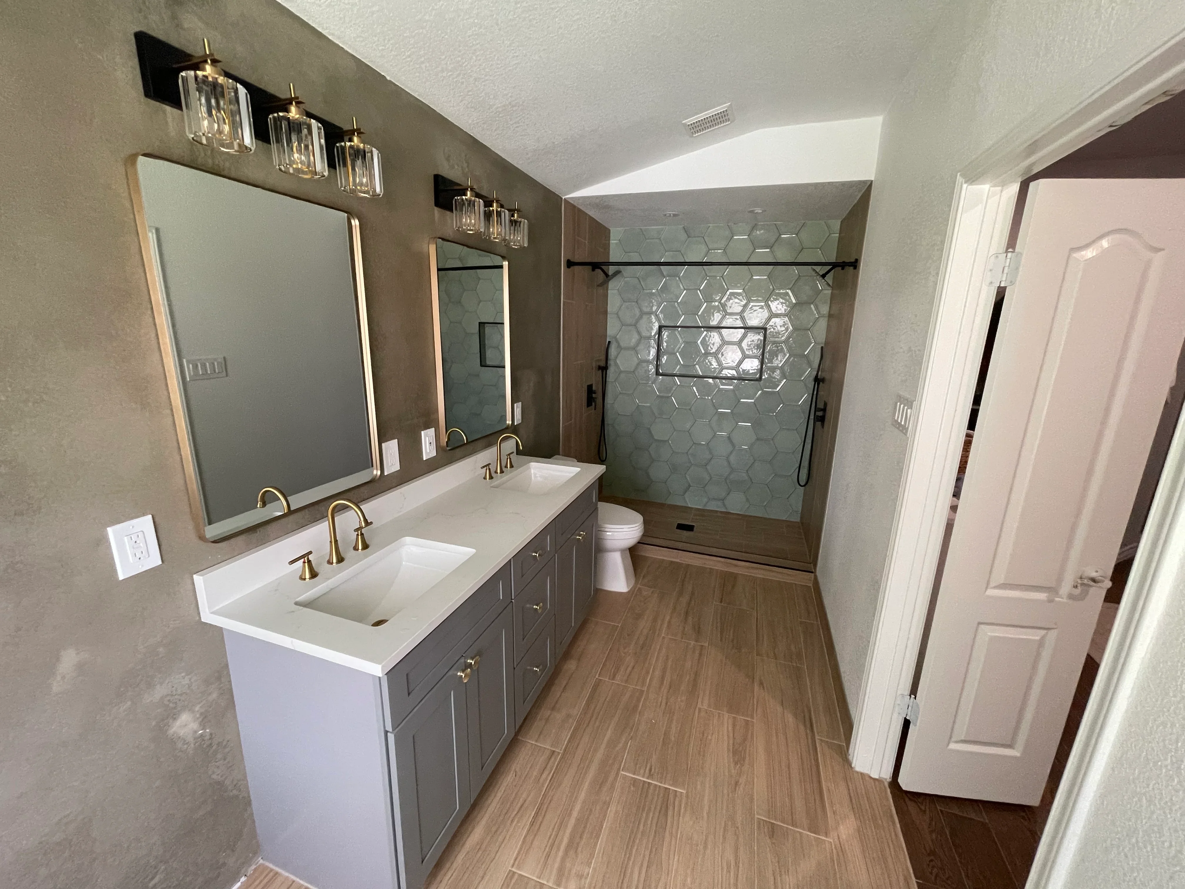 Bathroom with double vanity, quartz counters, hexagonal tile shower, wood flooring, and brass fixtures