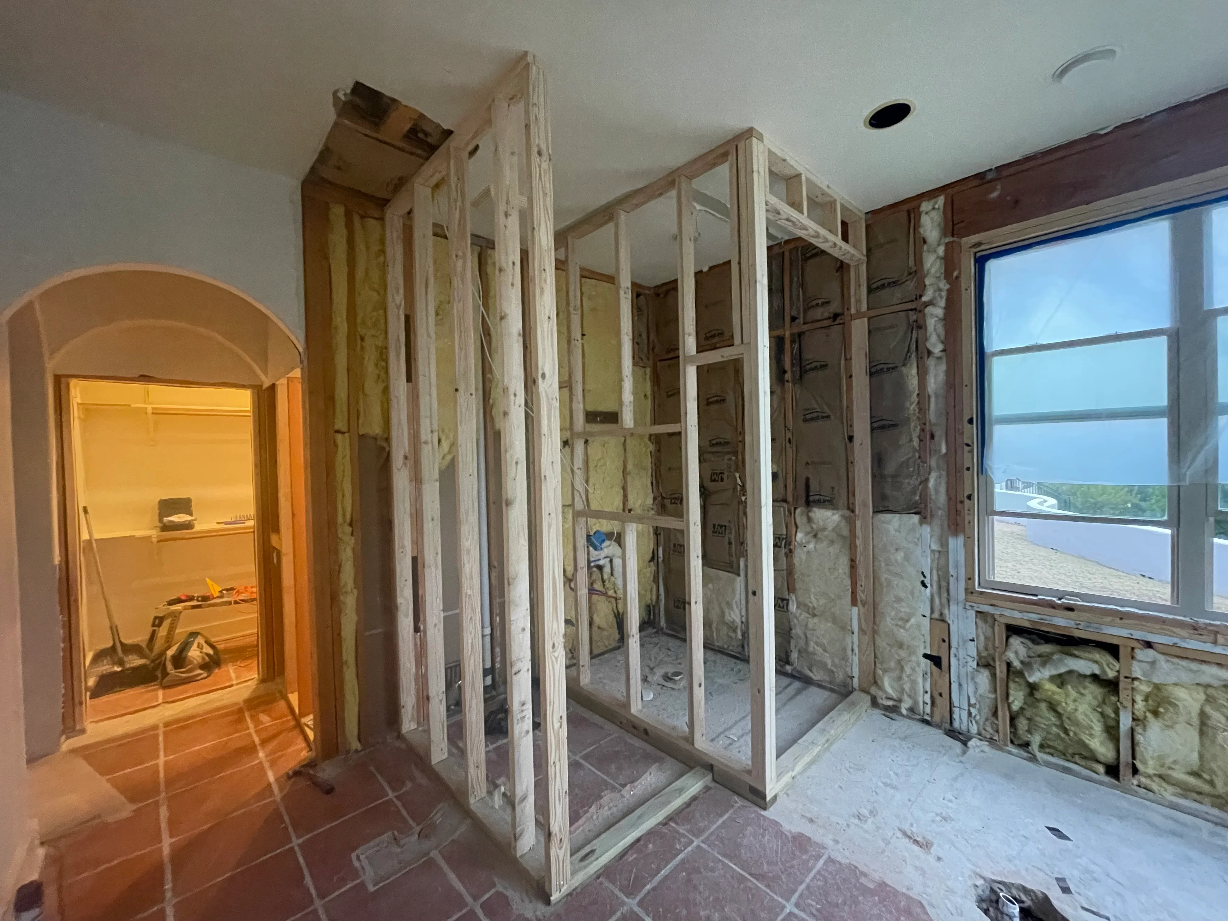 Bathroom framing with studs, insulation, arched doorway, and large window opening during construction