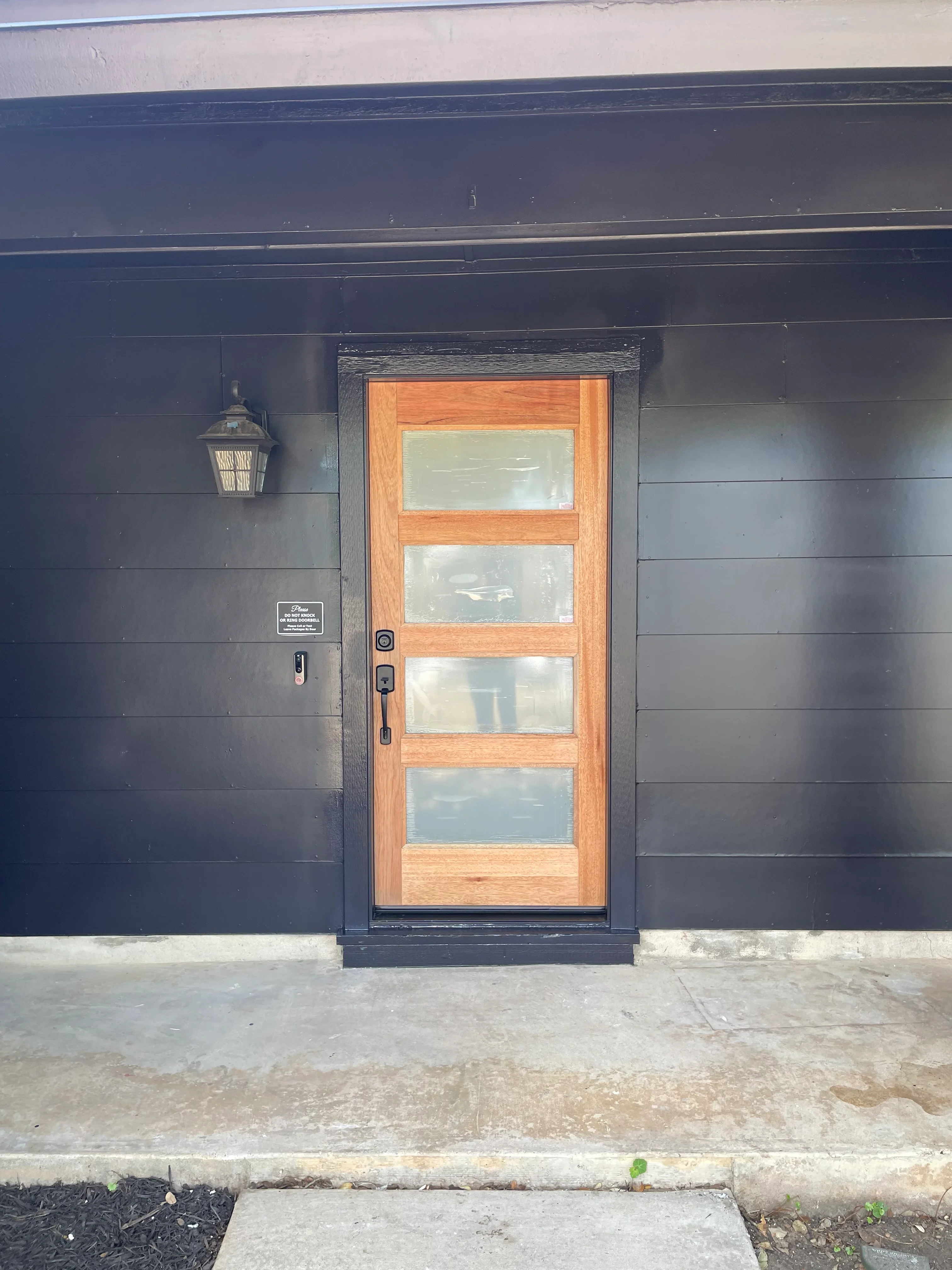 Custom wood-framed glazed entry door with five panels and dark steel surround on shiplap wall
