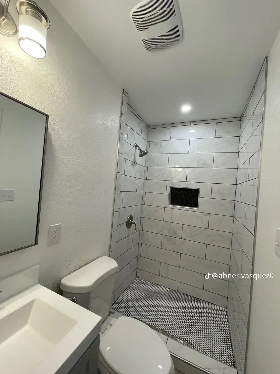Marble subway tile shower walls with black hexagonal floor tile and recessed lighting