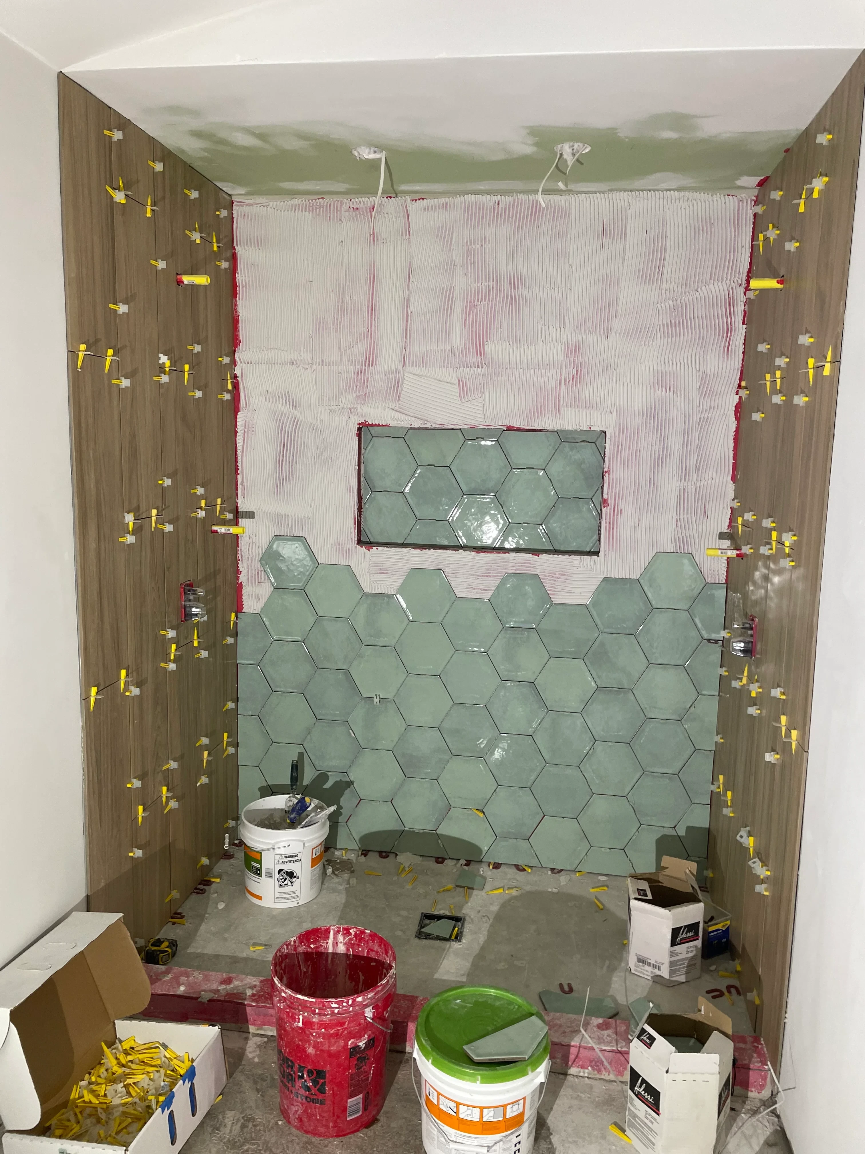 Bathroom under renovation with hexagon tile shower surround and wood plank flooring installation in progress