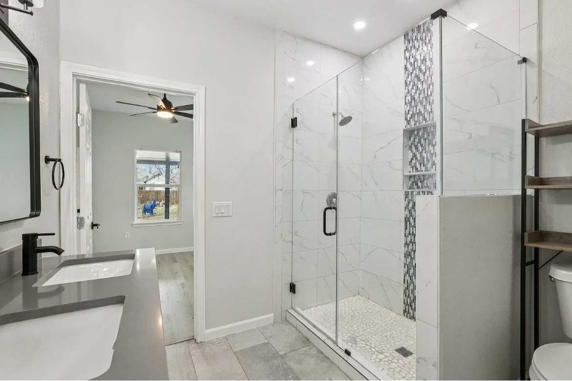 Modern bathroom with marble tile walls, frameless glass shower, and concrete countertops